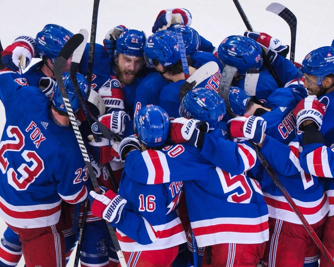 Several Rangers players celebrating on ice in Rangers uniforms after Barclay Goodrow's goal.