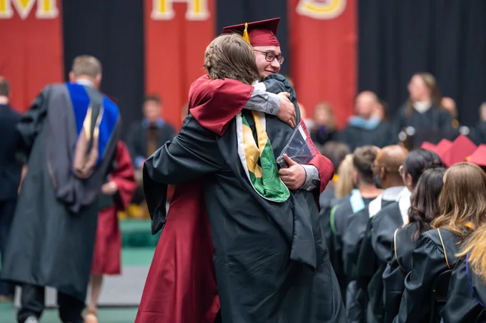 A student hugs a Rocky Mountain High School staff member at graduation.
