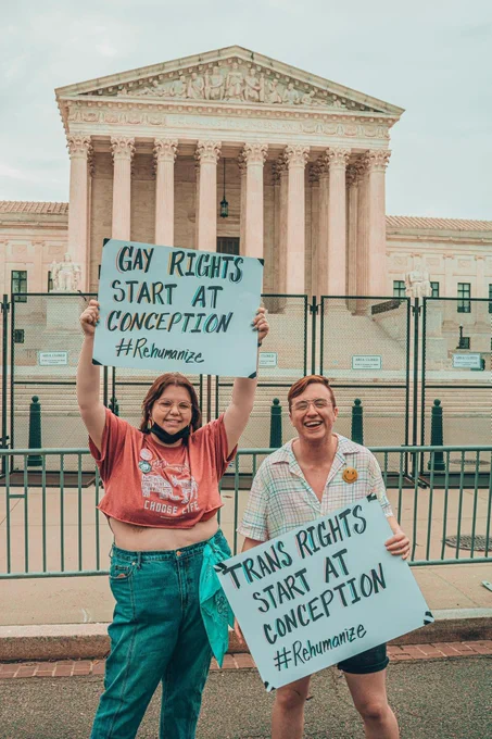 a photo of Kaine and Herb holding signs in front of the US Supreme Court that say “gay rights start at conception” and “trans rights start at conception.”