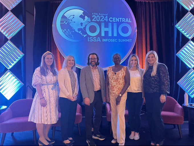 Six people posing on a stage in front of the 2024 COISSA InfoSec Summit banner.