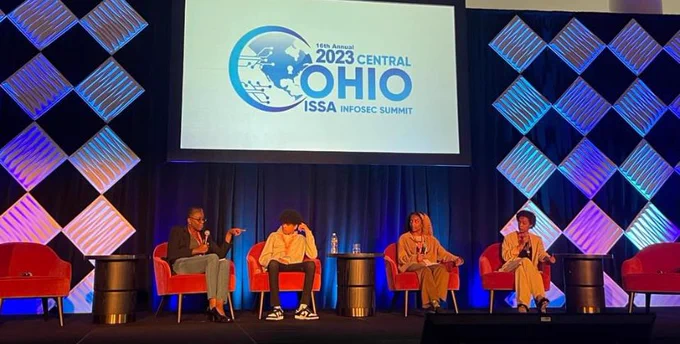 Four people seated on a stage in front of the 2023 COISSA InfoSec Summit banner.