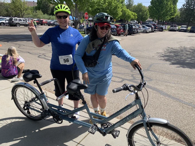 NWABA athlete and guide standing on a sidewalk holding their tandem bike and smiling at the camera.