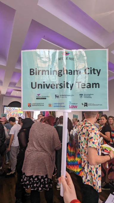Photo of a hand holding a banner saying “Birmingham City University team” There are people in the background