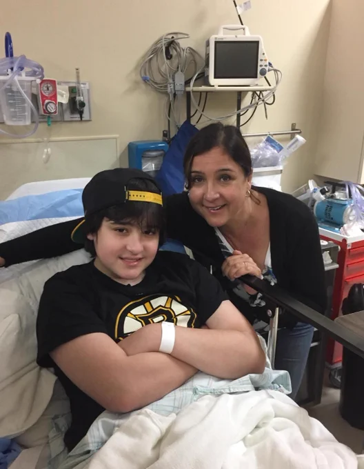 Photo of Donna leaning over the rail of her son's hospital bed with him smiling up at the camera