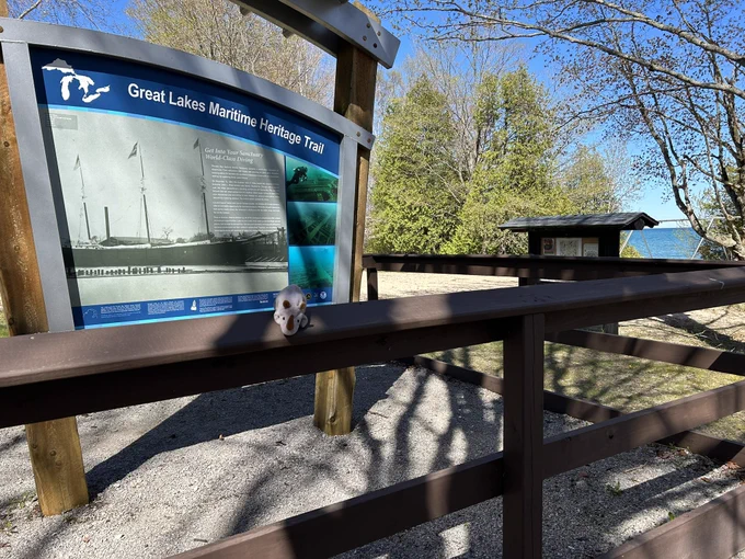 Small stuffed rhino on a wooden fence in front of a large sign with information about the Great Lakes Maritime Heritage Trail on it