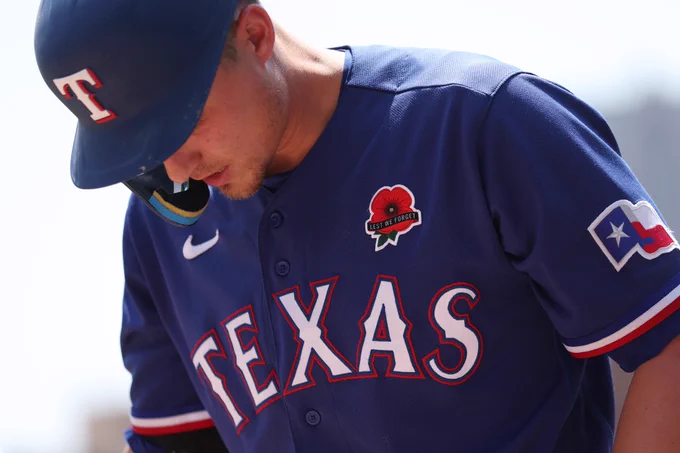Candid shot of Corey Seager in a blue Texas Rangers uniform. On his chest is a Memorial Day "Lest We Forget" remembrance poppy