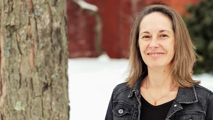 A woman (Allison) is standing beside a  tree. She is smiling at the camera.