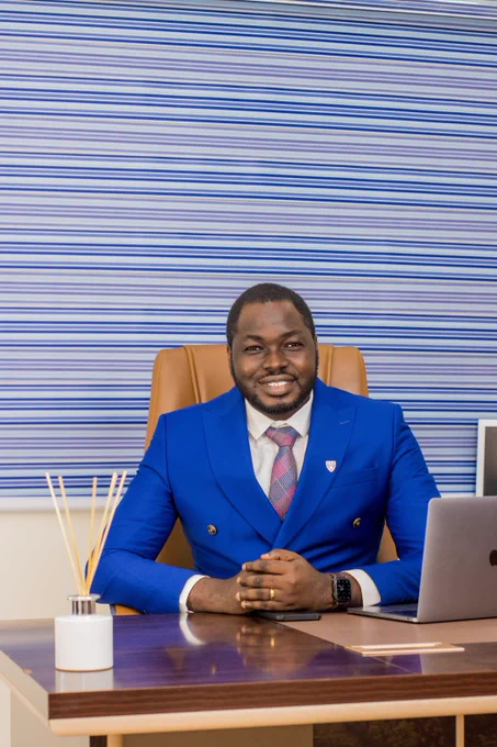 Ekundayo Ayeni sitting at a desk, smiling with arms resting on the table.