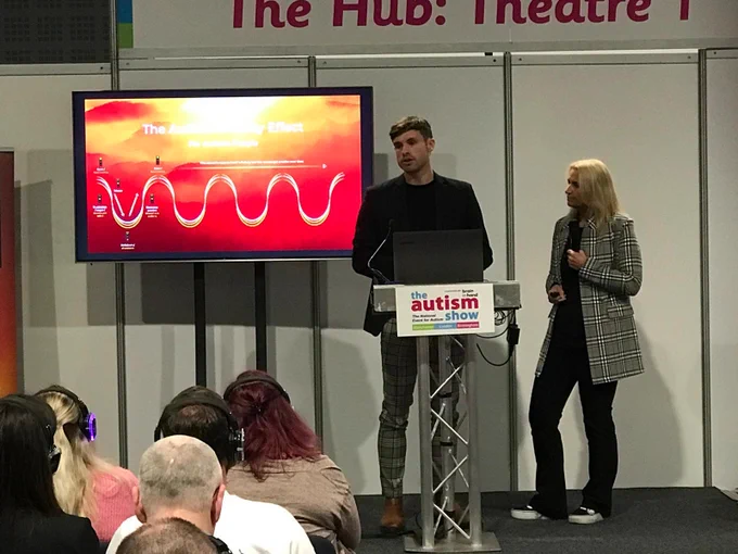 Caren and Callum on stage at the Autism Show in Manchester presenting their U-finity Effect of Autism Theory to an audience.