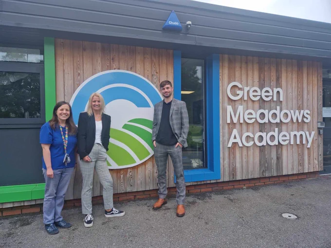 Caren Launus-Gamble and Callum Launus-Gamble standing in front of the school logo of Green Meadows Academy in Guiseley, Leeds with a member of staff.