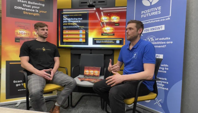 Callum Launus-Gamble & Wayne Stephenson at The Knowledge Exchange (TKE) at Leeds Beckett University sitting opposite each other in front of roller banners with their respective logos and a TV screen showing Callum's book.