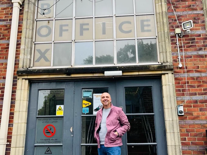 A person posing for a photo outside the Barry Memo entrance. A sign over the door reads: BOX OFFICE. 