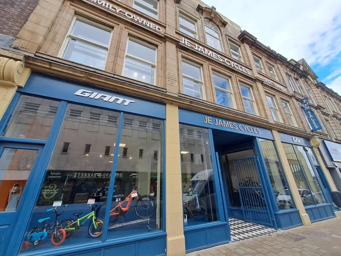 Traditional-style shop front within a three-storey historic building. There are bikes in the window and signage above the first floor windows that says 'Family owned, JE James, est. 1964' 
