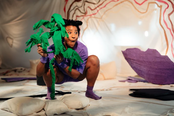 a performer dressed in purple holds a green puppet plant 