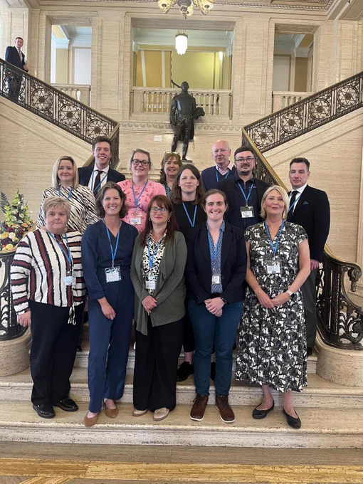 A group of people standing at the bottom of the grand stairs in Parliament Buildings, Stormont.