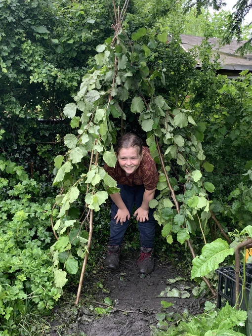 Photo of a young person crouching in a shelter made from hazel branches & leaves