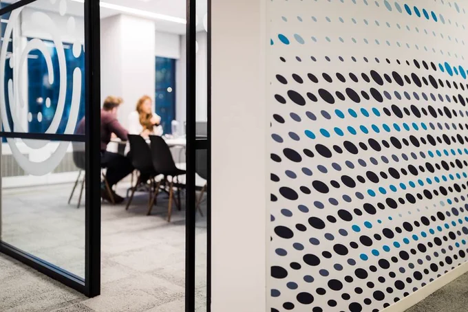 In the background, two colleagues sit in a meeting room having a discussion. This is out of focus, the Informa logos decorate the wall and glass wall which is the image feature