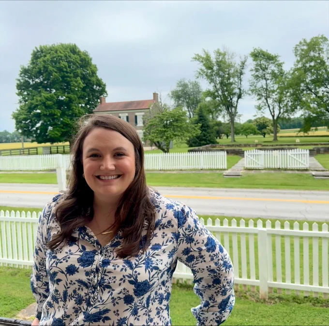 Image of Sally Givens Rogers standing in front of a white picket fence.