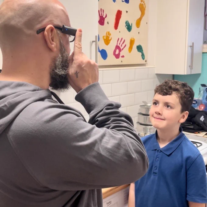 A man uses the OrCam MyEye's facial recognition feature to identify his young son, who is facing him.