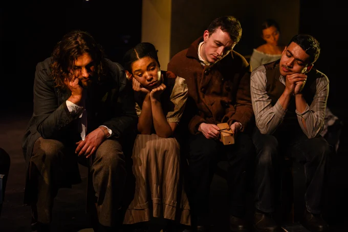 A group of actors sitting together on a bench, looking defeatedly at the floor