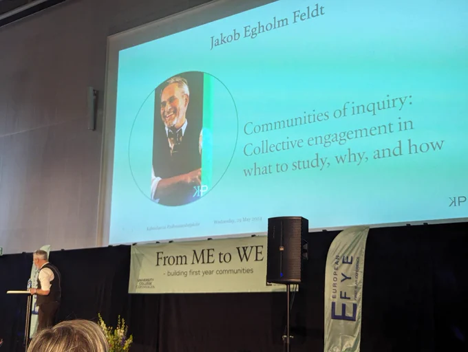 Picture of keynote speaker on a stage with background slide noting  "Communities of inquiry: collective engagement in what to study, why and how?"