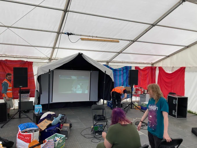 A tent, in a field, with a projector and a MASSIVE i mean MASSIVE sound system holy hells, also loads of junk, two people in high vis, and two people not in high vis