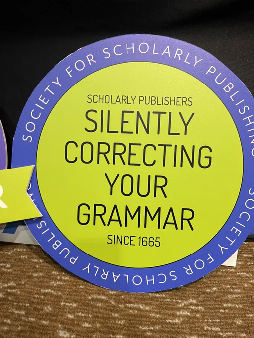 Round placard with "Society for Scholarly Publishing" printed around the edge; in the center is the slogan "Scholarly publishers: silently correcting your grammar since 1665."
