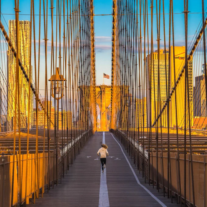 A photo of a person running over the Manhattan Bridge at sunset.