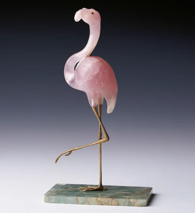 “Flamingo, carved from rose quartz with gilt-metal legs and feet, the eyes inset with rose diamonds, supported on a rectangular green quartz base.”