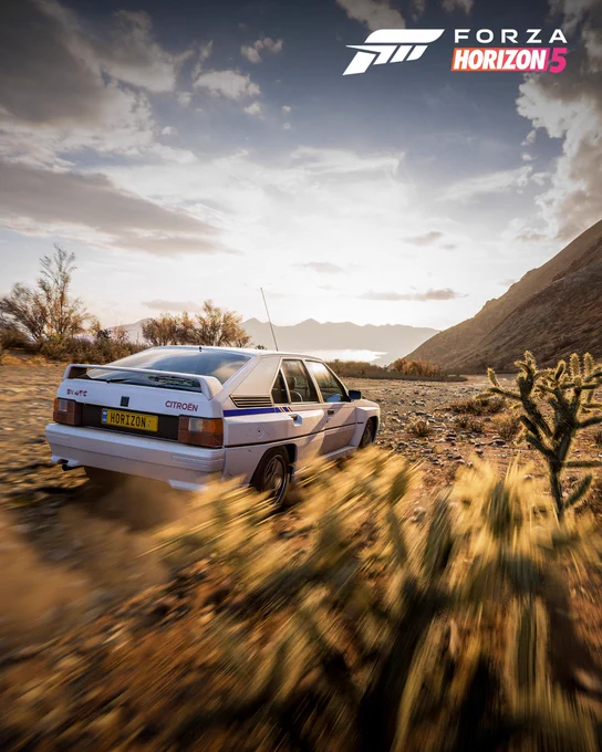 A Citroën BX 4TC racing through a desert landscape  with a mountainous background and clear sky.