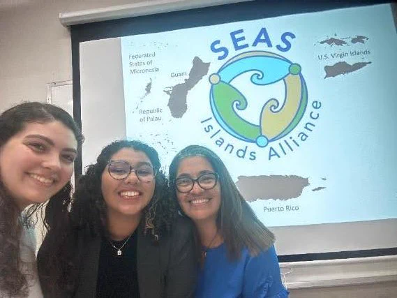 A selfie of Maria and two students in front of a SEAS Islands Alliance presentation.