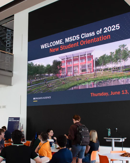 A group of students gathered inside the School of Data Science. "Welcome, MSDS Class of 2025 New Student Orientation” is displayed on a large media wall featuring an image of the School and the date, "Thursday, June 13.” 