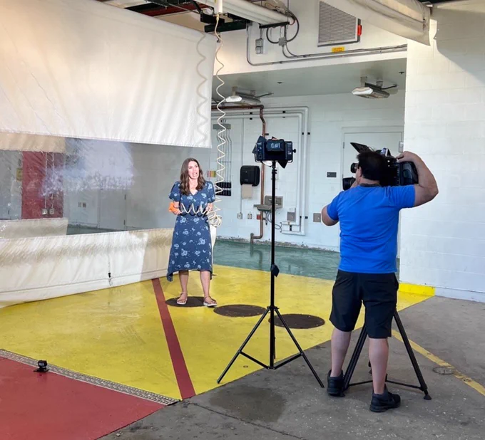 NBC Chicago reporter Lauren Petty stands in the Rush Emergency Department being filmed by another person with a video camera, with lighting equipment set up around them for a shoot.