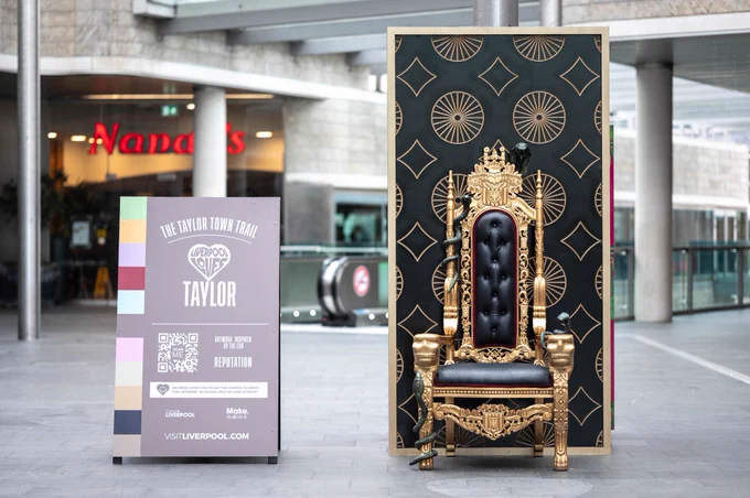 A gold throne with fake snakes on it and a black wall behind it.