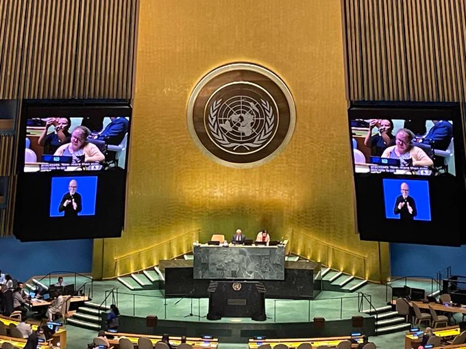 Mary Keogh is speaking on behalf of IDDC at the General Debate in the General Assembly Hall. She is featured on two screens in the background.