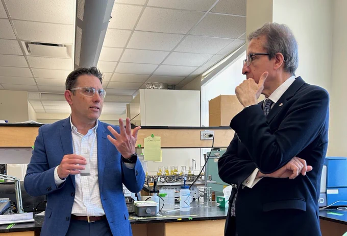  IMAGE: Two people standing in a laboratory in conversation. Science equitment on a table in the background. From left to right: Dr. Graham Gangnon, AlejandroAdem.