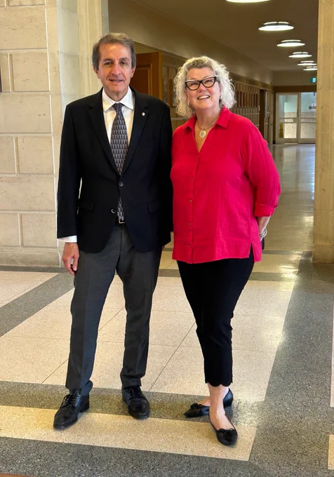 IMAGE: Two people standing in a university hallway smiling at the camera. Lockers in the back and large ceiling lights. from left to right: Alejandro Adem, Dr. Aiken.