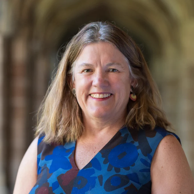 Professor Anne Kavanagh stands in the archways of the University of Melbourne, smiling at the camera.