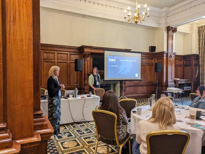 Two women give a presentation from the front of a room.