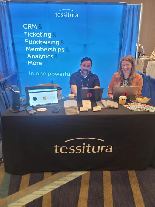 Kevin and Liz from Tessitura sitting behind a Tessitura-branded booth at the League of American Orchestras National Conference.