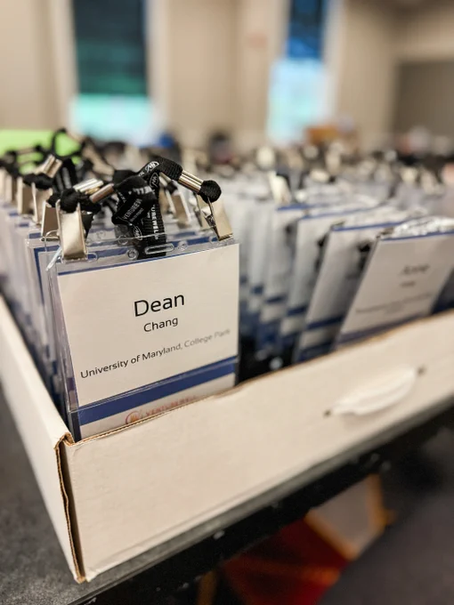 Rows of conference name tags displayed on a table, focusing on one that reads "Dean Chang, University of Maryland, College Park". The background shows more blurred tags and conference setting.