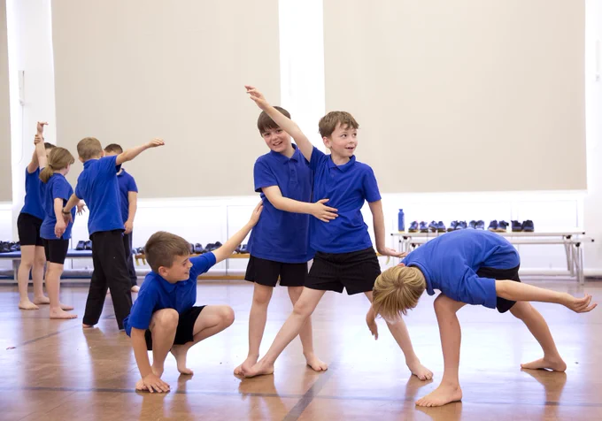 Two groups of children caught mid-movement. In the centre of the image are two boys standing in an upright pose with a boy connected on either side of the pair lower to the ground.