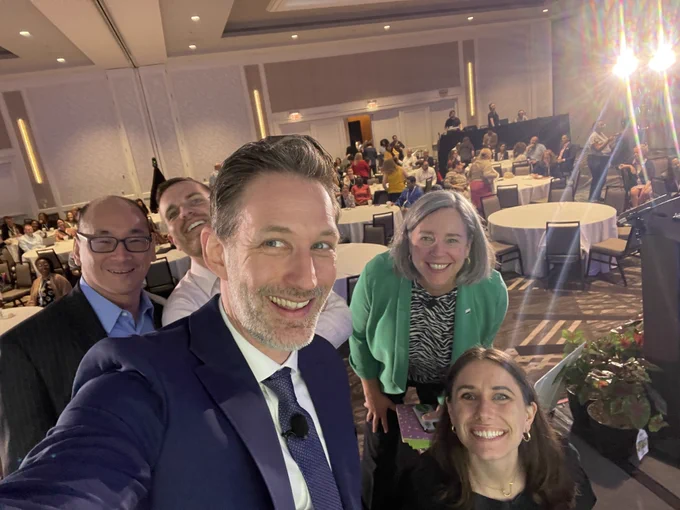 Five people take selfie in conference room. 