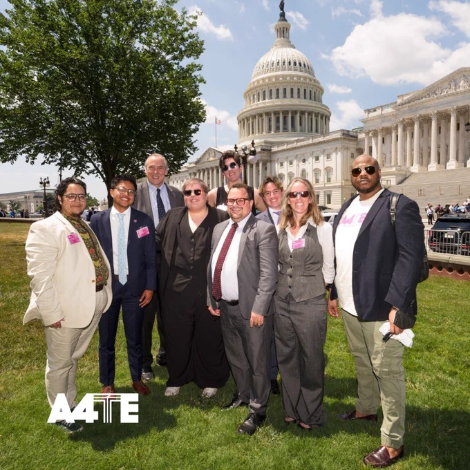 A diverse group of trans adovocates smile confidently at the camera while standing in front of the U.S. capitol.