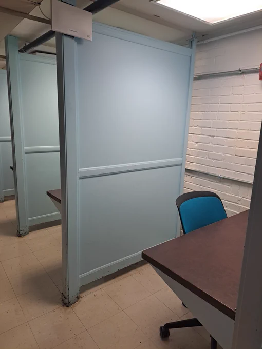 A row of desks with chairs and a blue screen dividing each one