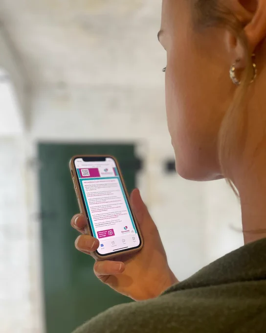 A person is looking at the Dementia UK website on an iPhone, focusing intently on the content displayed. There is a green door in the background.