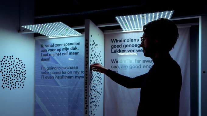 Tijdens de Places of Hope expositie stemt een persoon op een stelling over zonnepanelen en windmolens door een sticker te plakken.