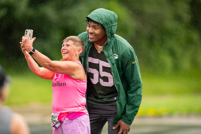 Two people taking a selfie in the rain, one in a pink top and the other wearing a green football jersey with the number 55.