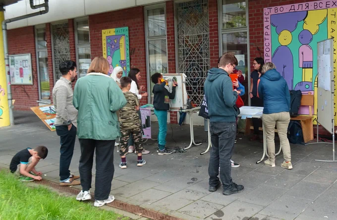 Menschen stehen in einem Stadtgebiet an einem Tisch mit Informationsmaterial und sprechen miteinander.
