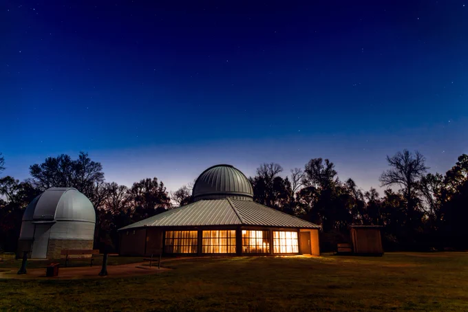 🪐🌙 Gather your Space Krewe for a stellar evening at Highland Road Park Observatory on July 5 at 8 PM for Edge of Night! 🌟🔭 Witness the first stars of the night, search for Mercury, Venus, and the Moon, and identify planes, satellites, and space debris as the sky transforms at twilight. 🌌✨ This FREE event is perfect for space enthusiasts of all ages. Don't miss out on this cosmic adventure! 🚀✨ 

Astronomy observatory at twilight with a starry sky above, featuring a large central dome and two smaller domes, all brightly illuminated from within.